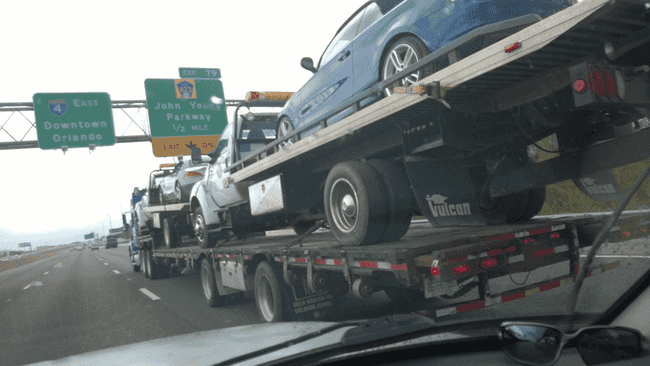 A tow truck, towing two tow trucks, each towing a car